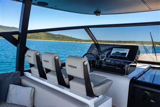 VanDutch 75 yacht helm with modern controls, overlooking serene blue waters and distant shoreline.