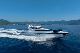 Mangusta 105 Sport 1999 yacht cruising on open sea with scenic coastline backdrop.