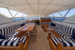 Luxurious 1999 Mangusta 105 Sport yacht interior with striped seating and wooden tables.