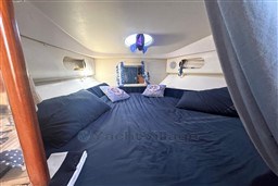 Cozy cabin interior of 2007 Mano Marine 24.50 with blue bedding and decorative pillows.