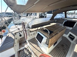 2011 Jeanneau 53 yacht cockpit with wooden table, steering wheel, and canopy in marina setting.