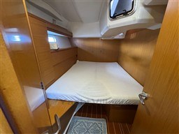 Cozy cabin interior of 2011 Jeanneau 53 yacht with wooden finish and bedding.