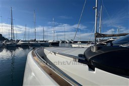 2023 Invictus TT 420 yacht docked in a marina with sailboats under a clear blue sky.
