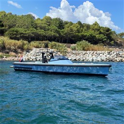 A 2004 Wally 45 boat on blue water near a rocky shoreline and lush greenery.