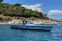Wally 45 yacht from 2004 cruising near a rocky shoreline with lush greenery.