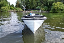 Corsiva 690 Tender boat on a calm lake with lush greenery and a windmill.