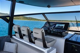 VanDutch 75 yacht helm with modern controls, overlooking serene blue waters and distant shoreline.