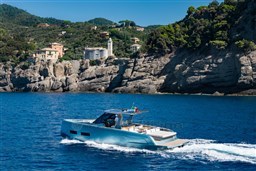 2026 Pardo Yachts 43 cruising near rocky coastline with lush greenery.