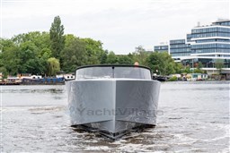 2024 VanDutch 40 yacht cruising on a river near modern buildings and lush greenery.